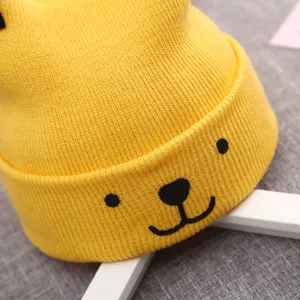 Close-up detail shot of cute yellow baby knit beanie featuring adorable embroidered bear face.
