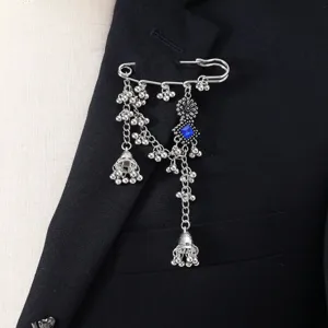 Close-up detail of silver bohemian tassel brooch with blue crystal and bells on black suit.