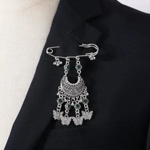 Close-up detail of bohemian vintage silver tone brooch with green gems and butterfly charms.