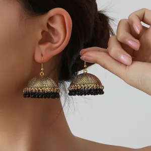 Close-up detail of vintage ethnic gold jhumka earrings with intricate filigree patterns.