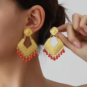 Close-up detail of vintage gold geometric rhombus earrings with red beaded tassels.