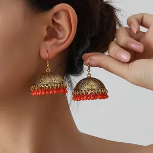 Detailed view of vintage ethnic style gold jhumka earrings with red bead fringe.