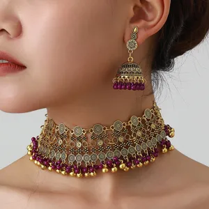 Close up detail of ethnic gold choker necklace and matching jhumka earrings with purple beads.