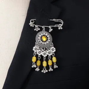 Primo piano dettagliato di spilla vintage in argento con strass e perline gialle su giacca.