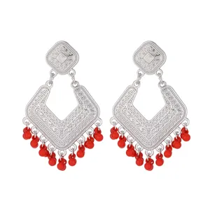 Close-up detail of retro silver-toned filigree drop earrings featuring vibrant red beaded fringe.