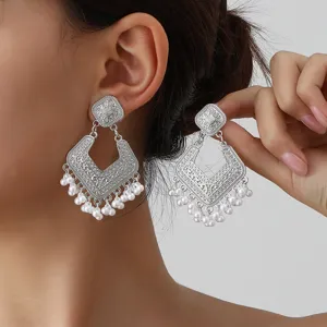 Close-up of vintage silver-toned geometric filigree drop earrings with delicate pearl tassels.