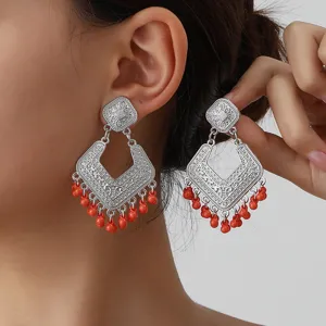 Close-up detail of vintage silver carved diamond-shaped earrings with red bead fringe.