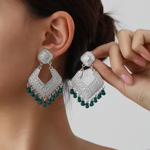 Close-up detail of retro silver geometric engraved earrings with green beaded tassels.