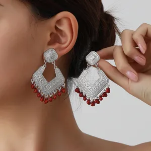 Detailed close-up of ethnic silver drop earrings featuring intricate carved patterns and red beads.
