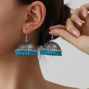 Close-up of vintage silver jhumka earrings with intricate engraved bell and blue bead fringe.