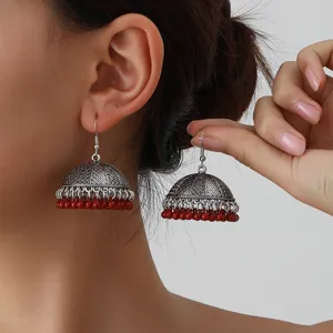 Close-up of vintage ethnic jhumka earrings with intricate silver carving and red bead fringe.
