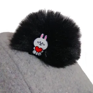 Cute children's hat detail view featuring a soft plush pom pom and adorable cartoon rabbit decor.