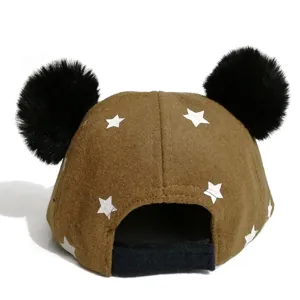 Detailed view of cute children brown star print baseball cap with black pom poms.