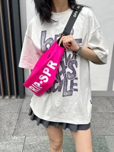 Detailed view of trendy pink crescent crossbody bag with bold white letters and strap.