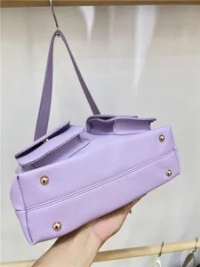 Close up of purple leather shoulder bag with utility pockets and gold metal bottom studs.