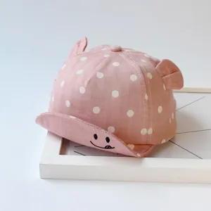 Close-up detail of cute pink polka dot baby baseball cap featuring playful ears and smile.