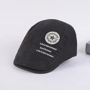 Detail view of dark grey cotton flat cap with embroidered fashion badge and lettering text.