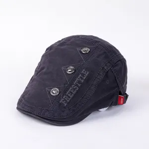 Close-up detail of dark grey flat cap with metallic button decorations and embroidery.