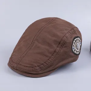 Close-up of brown cotton flat cap, vintage newsboy hat detail with side embroidered badge.