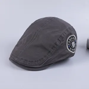 Close-up detail of the dark grey cotton flat cap with side embroidered fashion patch style.