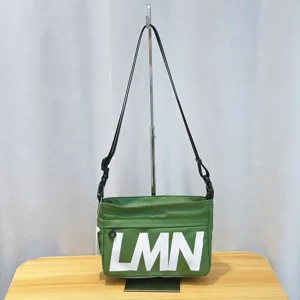 Green crossbody bag detail showing large LMN print and adjustable black shoulder strap.