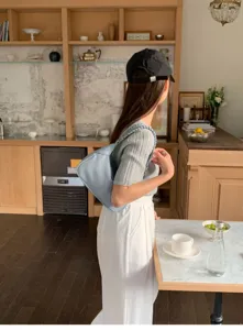 Detailed lifestyle view of a minimalist light blue shoulder bag worn by a model in a cafe.