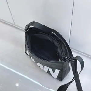 Black waterproof shoulder bag with large letter design, casual crossbody pillow bag detail.