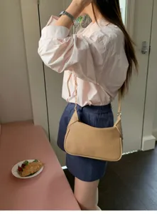 Detail view of the beige minimalist shoulder bag worn casually, showcasing its sleek strap design.