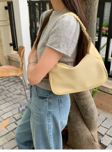 Detail view of minimalist yellow hobo shoulder bag with stylish braided strap in lifestyle setting.