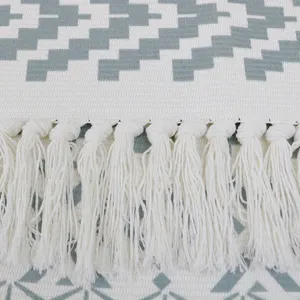 Close-up detail of the woven cotton rug showing soft white fringe and grey geometric patterns.