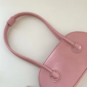 Pink shoulder bag detail view showing long handle and shell design for women's fashion.
