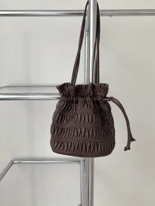 Detail shot of a dark brown pleated drawstring shoulder bag hanging on a chrome rack.