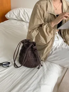 Detail view of the dark brown ruched drawstring bucket bag on a clean white bed setup.