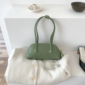 Close-up detail of a chic green shoulder bag featuring long handles on a clean white set.