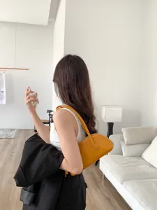 Detail view of minimalist yellow leather underarm shell bag with comfortable long strap in interior.