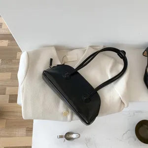 Close-up detail shot of the black patent leather underarm bag, showcasing the smooth strap design.