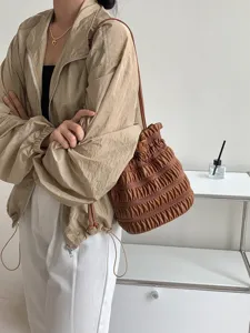 Detail shot showing the brown ruched drawstring bucket bag worn on shoulder with neat pleats.
