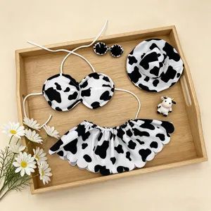 Cute cow print bikini set with top, skirt, hat and sunglasses for summer beach wear.