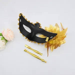 Black and gold masquerade mask with detachable handle, feather and flower decorations.