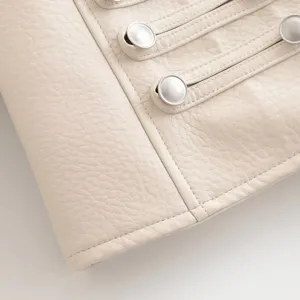 Gros plan sur les details de la veste en faux cuir beige avec boutons metalliques et coutures.