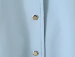 Light blue trench coat detail view featuring smooth fabric and silver metal snap buttons.