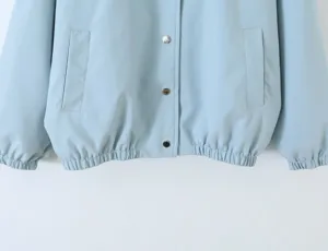 Light blue jacket detail shot featuring metal snap buttons and functional side pockets.