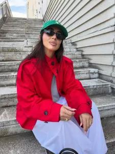 Detail view of the stylish red pocket trench coat jacket worn outdoors on stone stairs.