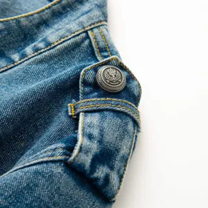Close-up view of denim jacket shoulder, showing contrast yellow stitching and ornate metal button.