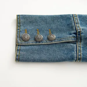 Close-up of denim jacket sleeve cuff featuring vintage metal crest buttons and stitching.