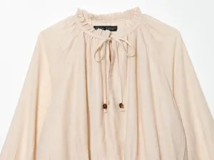 Ruffled collar beige blouse detail with drawstring and wooden beads, elegant apparel close-up.