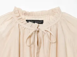 Beige blouse collar detail, ruffled mock neck with front tie strings, soft textured fabric close-up.