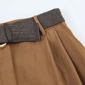 Detalle de pantalones cortos plisados de talle alto marrones con elegante cinturón tejido oscuro.