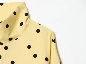 Close-up detail of yellow high neck top with black polka dots, soft fabric texture.