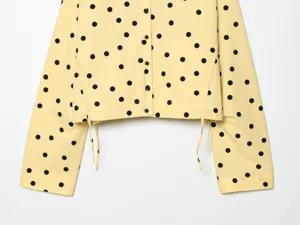 Detailed shot of women's yellow long sleeve jacket featuring classic black polka dots and buttons.